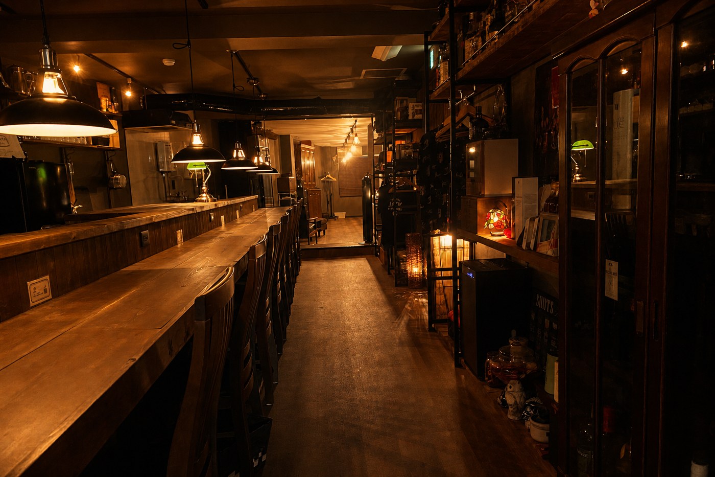 夜の店内。ペンダントランプに照らされた木のカウンター席と、奥に並ぶ酒棚